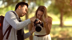 Male photographer showing a female subject a photo on the back of his DSLR camera outdoors.