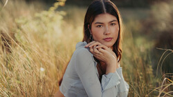 Young woman in light blue shirt posing in golden grass field during golden hour.
