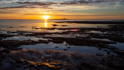 Golden sunset reflecting across rocky tidal flats and shallow pools at low tide.