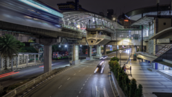 Nighttime urban street scene with elevated highway overpass, wet pavement, and blurred vehicle lights.