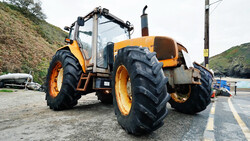 Yellow and black agricultural tractor with large treaded tires parked on a paved road near hillside terrain.