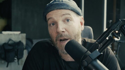 Person speaking into a large-diaphragm microphone in a studio setting with surprised expression.