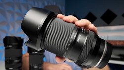 A telephoto zoom lens with lens hood held in a hand, displaying distance scale markings and aperture settings.