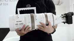 Photographer holding a white Viltrox 42-420mm zoom lens with visible focus and aperture rings.