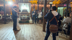 Bride and groom first dance at indoor wedding reception with guests watching from wooden floor venue.
