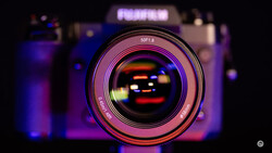 Close-up of a 50mm f/1.8 camera lens with purple and orange bokeh lighting in the background.