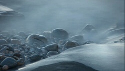 Snow-covered boulders shrouded in mist along a frozen coastline.