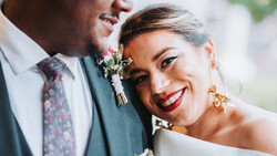 Bride and groom smiling closely together, with bride wearing red lipstick and gold earrings.