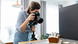 Photographer holding a professional camera with telephoto lens on a tripod while composing a food still life shot.