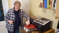 Photographer displaying printed photographs and photo book next to a desktop printer.