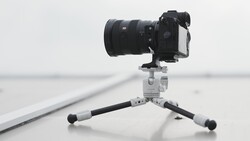 Mirrorless camera with telephoto lens mounted on a compact tripod against a minimalist gray background.