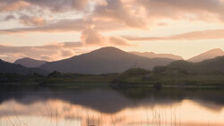 Mountain landscape reflected in still water at golden hour with warm, diffused light.