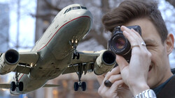 Photographer using telephoto lens with commercial aircraft in flight overhead.