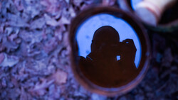 Silhouette of photographer holding camera visible through circular opening in textured wall.