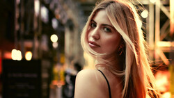 Woman with long reddish-blonde hair looking over shoulder in urban evening setting with warm city lights.