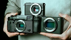 Three mirrorless cameras held in hands, showing sensor sizes from smallest to largest.