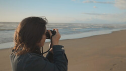 Woman photographing the ocean from a beach during golden hour.