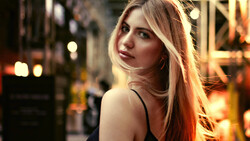 Woman with long reddish-blonde hair photographed outdoors at night with warm city lights in background.