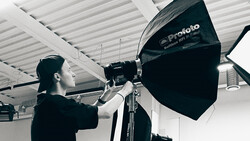 Photographer adjusting a large black Profoto softbox mounted on a light stand in a studio with white ceiling.