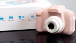 Pink compact digital camera with white lens barrel displayed next to its product packaging box.
