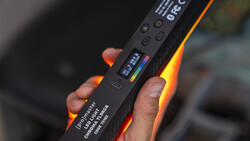 Hand holding a black lighting panel with illuminated orange-red edge lighting and a small display screen.
