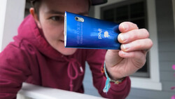 Person in burgundy hoodie holding blue smartphone displaying its rear case and camera.