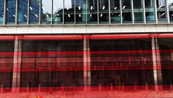 Modern building facade with vibrant red-tinted glass panels reflecting surrounding architecture and sky.