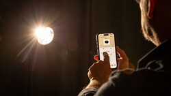 Photographer holding smartphone while composing a shot of a bright studio light fixture.