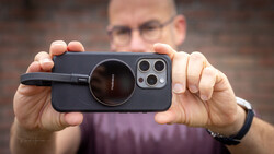 Man holding iPhone with black magnetic lens attachment, displaying triple camera setup.