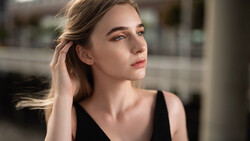 Woman in black tank top looking away, hand near ear, soft natural lighting from the side.