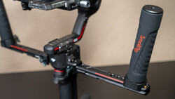 Gimbal stabilizer with extended arm grip mounted on table, with motorized gimbal head visible in background.