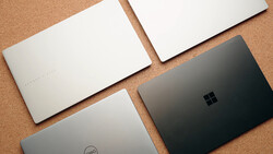 Four laptop computers arranged on a cork surface, showing their closed lids from above.