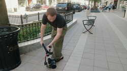 Photographer bending down to adjust a camera mounted on a skateboard on an urban sidewalk.