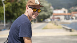 Man wearing a brown cap and yellow-tinted sunglasses smiles at the camera outdoors.