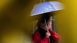 Woman in red jacket holding transparent umbrella against yellow background.