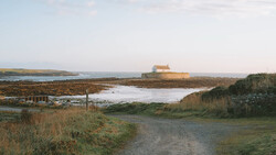Isolated stone building with orange roof on distant headland overlooking tidal marshland and mudflats.