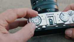 Hands holding a Fujifilm rangefinder camera with film advance dial visible and XF lens mounted on top.