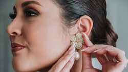 Woman in profile adjusting a pearl and crystal cluster earring near her ear.