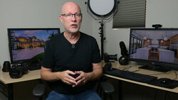 Man in black shirt seated at desk with dual monitors displaying architectural renderings.