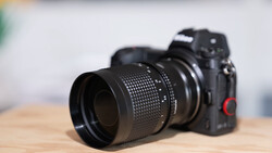 A telephoto lens mounted on a mirrorless camera body with red accents, displayed on a wooden surface.