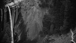 Waterfall cascading down a rocky cliff face surrounded by dense forest in black and white.