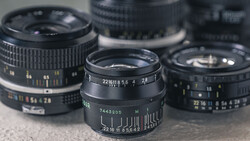 Three vintage manual focus lenses with aperture and focus rings visible, arranged on a neutral surface.