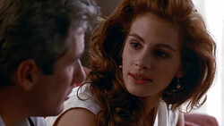 Woman with reddish-brown wavy hair in close conversation with a man, soft intimate lighting and shallow depth of field.