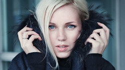 Portrait of a woman with platinum blonde hair and dark eye makeup holding black feathered props near her face.