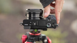 Sony a6100 mirrorless camera held in hand with attached lens, showing top controls and 4K capability marking.