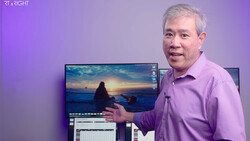 Man in purple shirt demonstrating photo editing workflow with sunset landscape image on monitor.