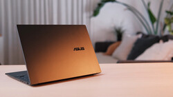 ASUS laptop with copper-colored lid angled on desk, blurred background with potted plant and desk accessories.