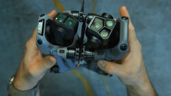 Overhead view of hands holding a drone remote controller with dual control sticks and illuminated button interface.