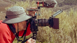 Videographer filming outdoors with professional cinema camera rig and mounted microphone.