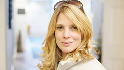 Woman with shoulder-length blonde hair wearing sunglasses on her head, looking at camera with neutral expression.